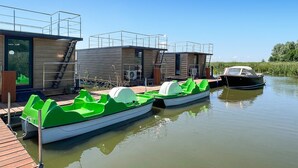 Une rangée de maisons flottantes modernes et compactes, dotées d’escaliers extérieurs, reliées par une jetée en bois.