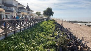 Une promenade en bord de mer, dotée d’une rambarde en bois, qui mène à une plage protégée par une digue rocheuse.