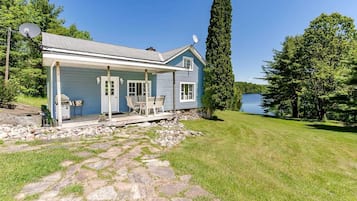 Situated on a grassy area with a view of a lake, this house features a covered porch and a stone pathway leading to the entrance.