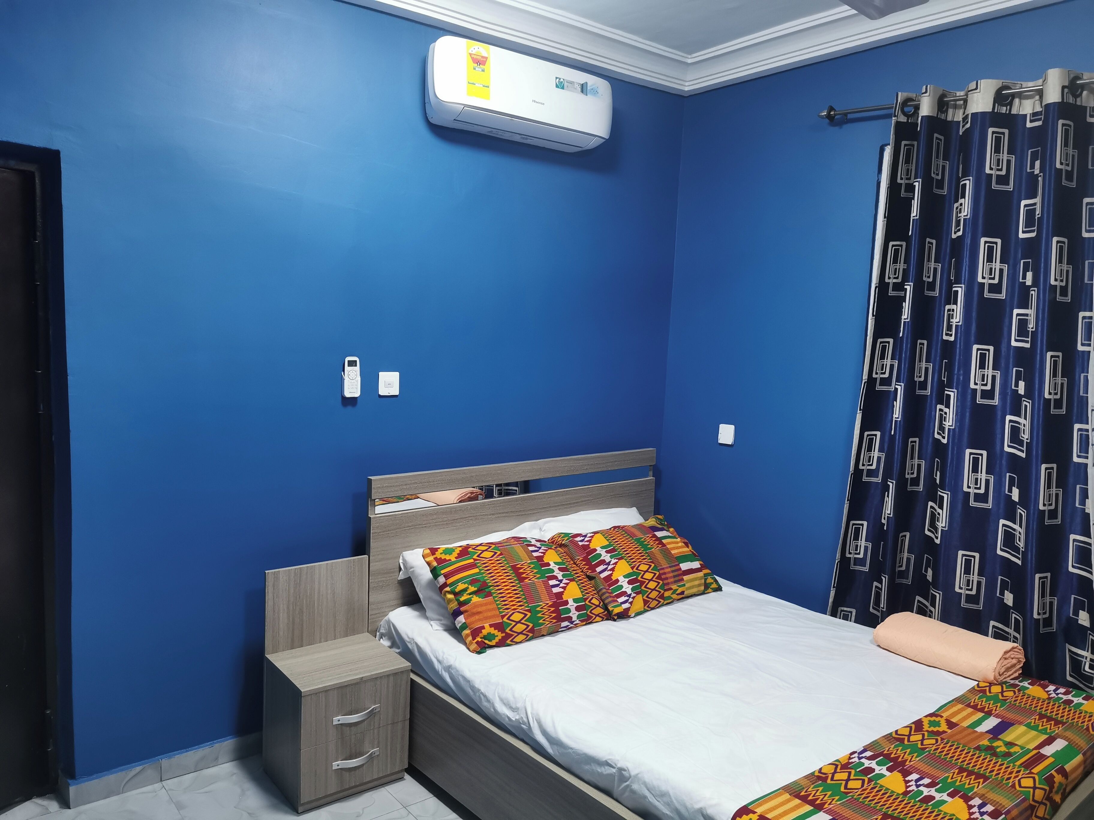 A bedroom with a bed, a bedside table, a wardrobe, a wall-mounted air conditioner, and a curtain.
