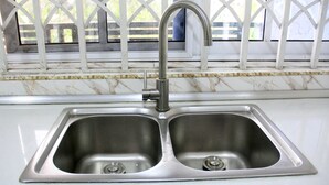 A kitchen with a double stainless steel sink, a faucet, and a window with a white frame. - Tropical Oasis in Accra - 2 Bedroom Apartment (Accra)