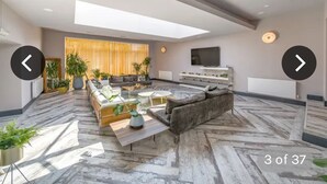 Un salon moderne avec un canapé, une table basse et des plantes. Un téléviseur est fixé au mur et il y a une fenêtre avec des rideaux.