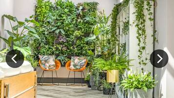 Hotellihuone, jossa on kalanruotokuviollinen lattia, puinen sänky, kaksi oranssia tuolia ja seinä, joka on peitetty erilaisilla kasveilla.