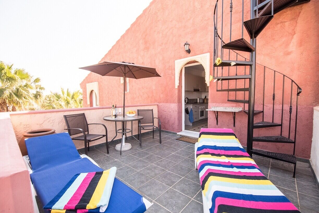 Una terraza en la azotea con sillones de descanso, una mesa y una escalera de caracol.