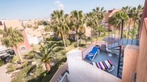 A balcony with a view of a residential area, palm trees, and a swimming pool area with lounge chairs. - SunRays  Naturist Apartment in Playas de Vera (Playas de Vera)