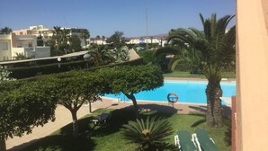 A pool area with lounge chairs, palm trees, and a clear blue sky. - SunRays  Naturist Apartment in Playas de Vera (Playas de Vera)