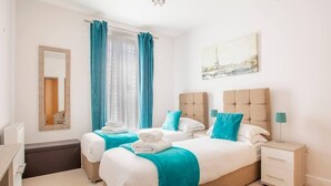 Una camera d'albergo con due letti, un comodino con lampada, uno specchio e una finestra con tende.