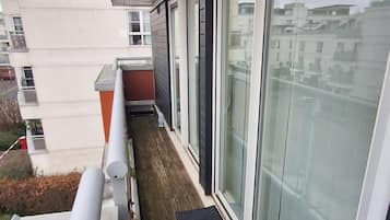 A balcony with a wooden floor, a black mat, and a glass door leading to a room.