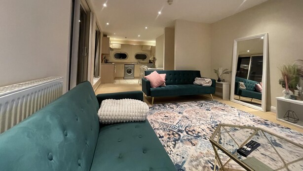 A modern living room with a teal sofa, a patterned rug, and a small coffee table. - Free parking near city centre & stadium sleeps 6-8 (Leicester)