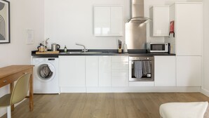 A modern kitchen with white cabinets, a washing machine, a microwave, and a wooden table.