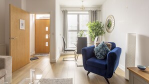 A modern living room with a blue armchair, a wooden door, a dining area, and a large window with curtains.