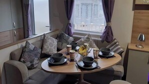 A dining area with a round table set for four, a sofa with cushions, and a view of a building through the window.