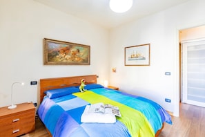 A bedroom with a bed, a nightstand, a lamp, a painting, and a door. - Appartamento Le Mimose In Lucca, Lucca, Italy (Lucca)