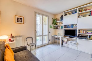 A living room with a sofa, a TV, a bookshelf, and a dining area with chairs. - Appartamento Le Mimose In Lucca, Lucca, Italy (Lucca)