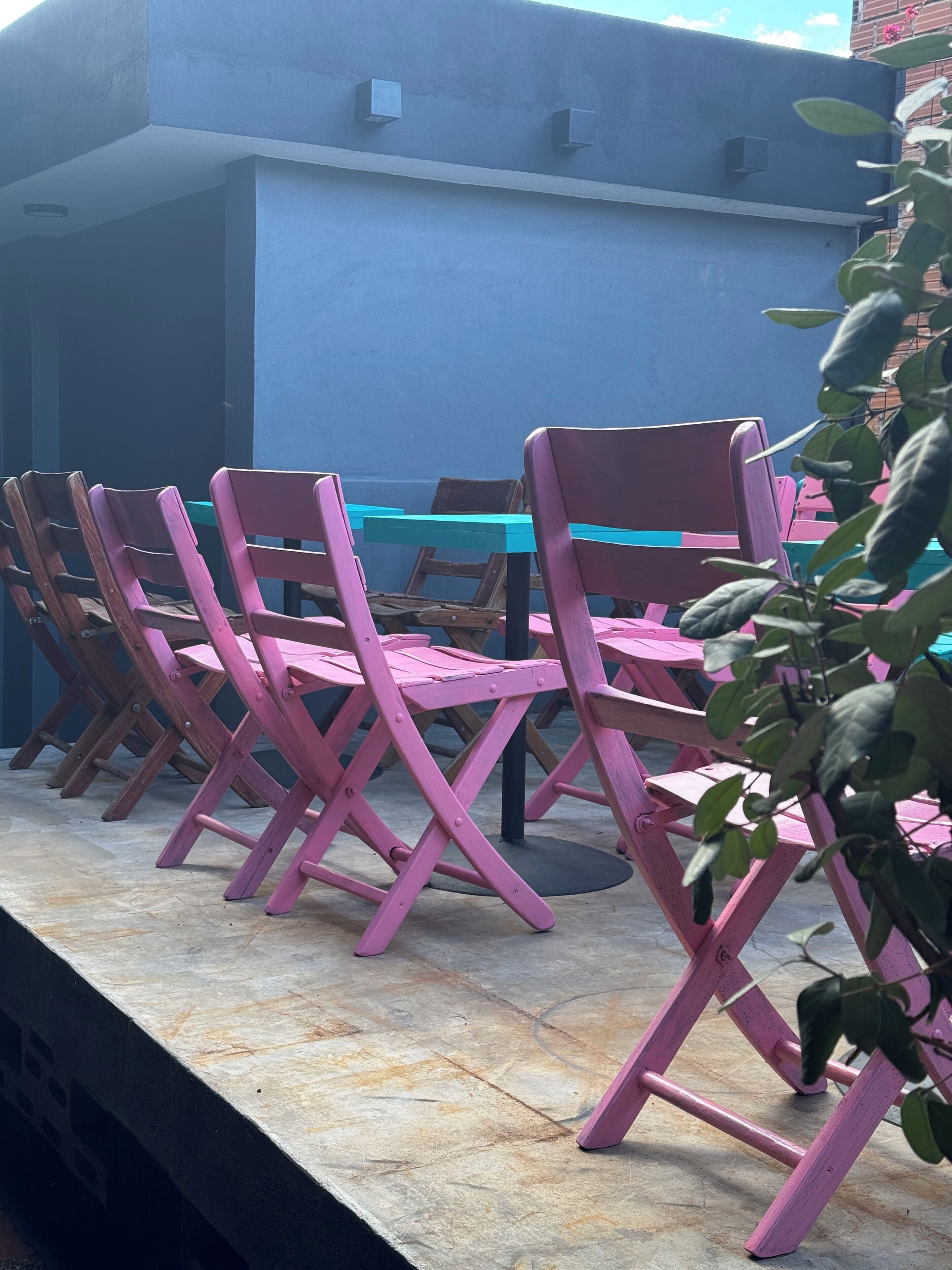 A row of pink folding chairs with a blue table in an outdoor patio area.