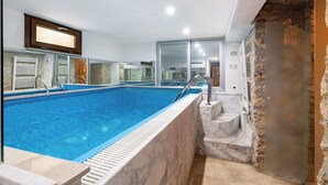 Una piscina con borde de mármol, pared de piedra y televisor sobre ella.