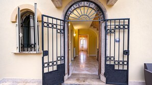 Un pasillo con un gran arco, una ventana con reja metálica y suelo de baldosas.