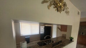 Una cocina con encimera de granito, pileta de acero inoxidable y ventana con persianas.