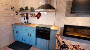 Een compacte keuken met blauwe kastjes, een zwart fornuis en een wandgemonteerde flatscreen-tv.