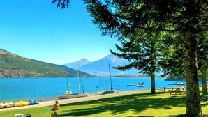 Vista de un lago con barcos, un área con césped y montañas al fondo.