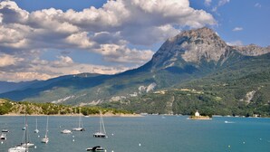 Un paisaje costero con una montaña, barcos y una pequeña isla con un edificio blanco.