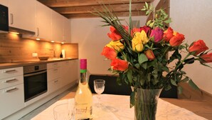 Een keuken met witte kastjes, een houten plafond, een wijnfles en een vaas met bloemen op een tafel.