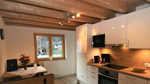 Een moderne keuken met houten balken, witte kastjes, een ingebouwde oven en een raam met uitzicht op een huis.
