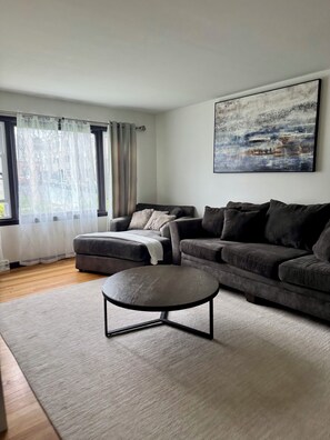 A modern living room with a grey sofa, a round coffee table, and a large abstract painting on the wall.