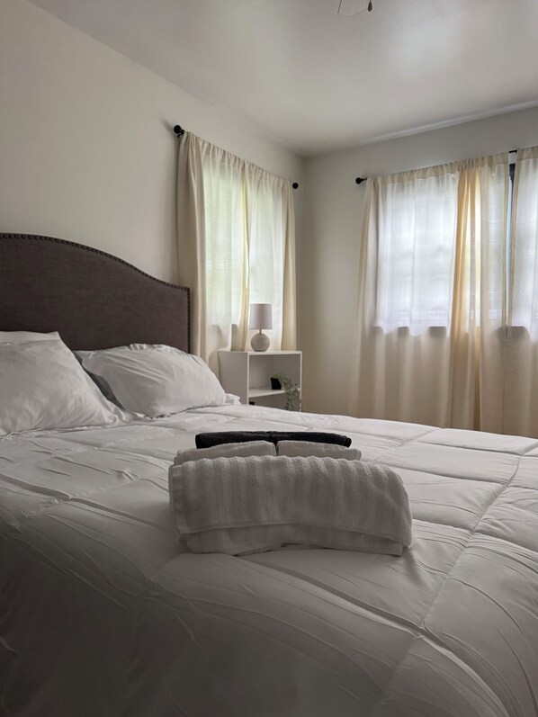 A neatly made bed with white linens, a dark headboard, and a bedside table with a lamp.