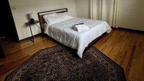 Un dormitorio con una cama, una mesita de noche, una lámpara, una luz de techo y un tapete estampado.