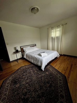 A bedroom with a bed, a nightstand, a lamp, a ceiling light, and a patterned rug.