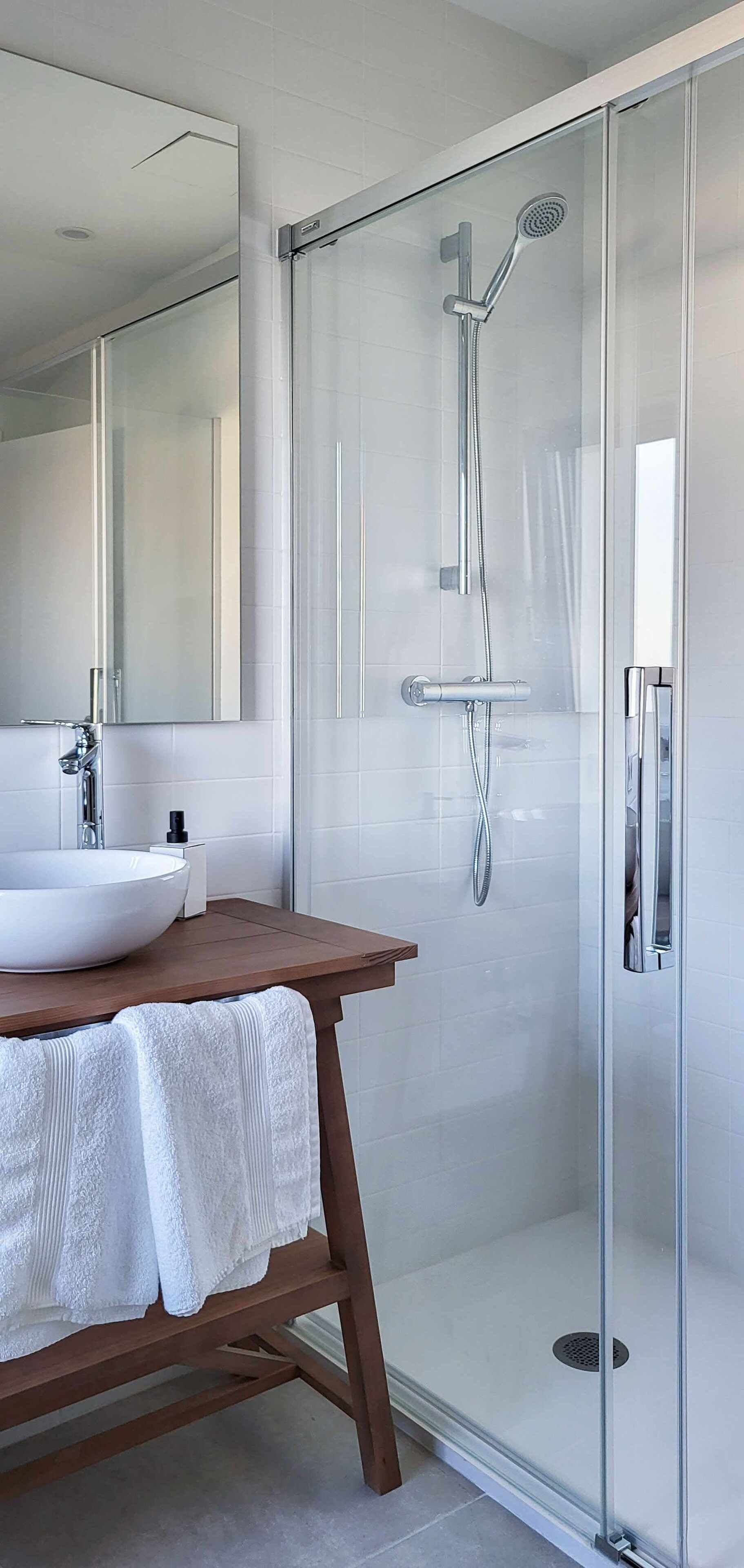 Ein modernes Badezimmer mit einer Duschkabine, einem Holzbadezimmermöbel mit Waschbecken in Weiß und einem großen Spiegel.