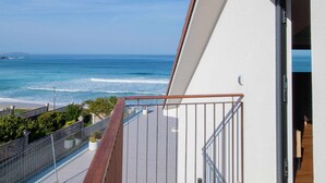 Uma varanda com vista para o oceano, um corrimão de madeira e uma porta que dá para um quarto.