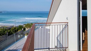 A balcony with a view of the ocean, a wooden railing, and a door leading to a room.