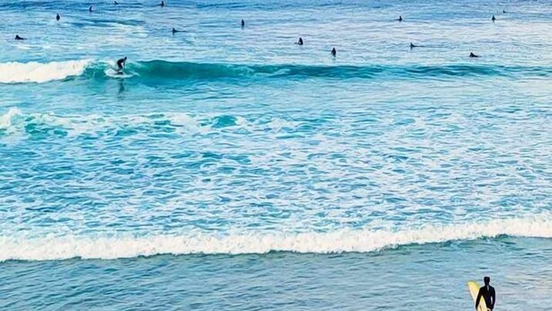 A beach with surfers in the water and one standing on the shore with a surfboard.