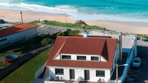 A modern two-story house with a red roof, a well-maintained lawn, and a view of the ocean.