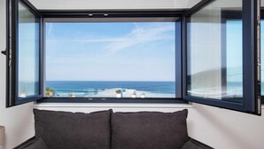 A room with a large window overlooking the ocean, a dark gray sofa, and a small table with a lamp.