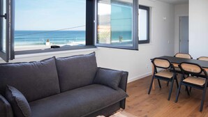 Una habitación moderna con un sofá gris, una mesa de comedor con sillas y vista al océano.