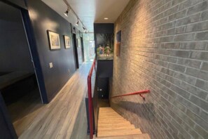 A hallway with a wooden floor, a red handrail, and a brick wall.