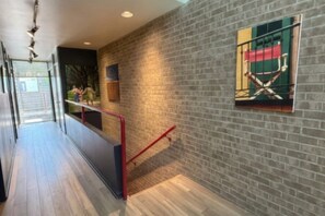 A hallway with a brick wall, a red railing, and a window with a view of a green landscape.