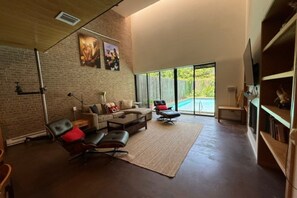 A spacious living room with a large window, a brick wall, and a pool visible through the glass doors.