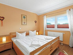 A hotel room with a wooden bed, white linens, a nightstand with a lamp, a window with blinds, and a radiator.