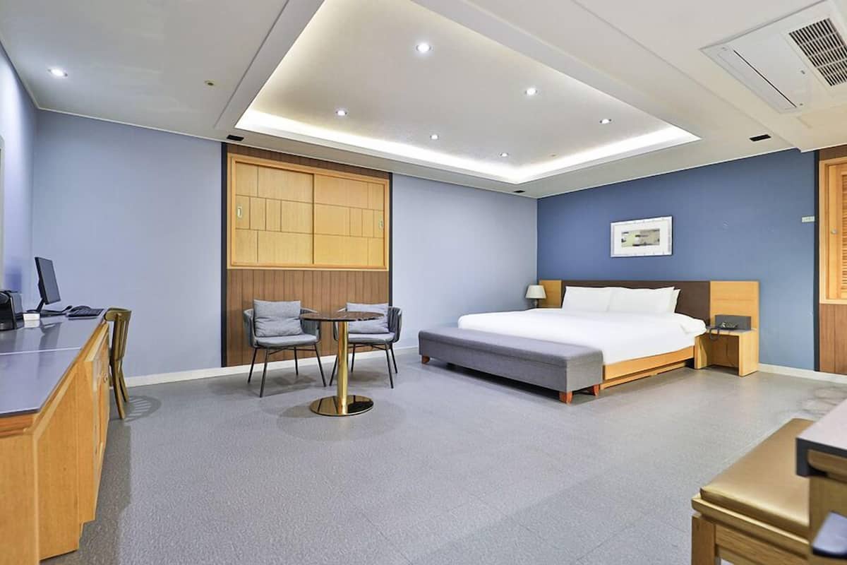 A modern hotel room with a bed, desk, chairs, and a small table.