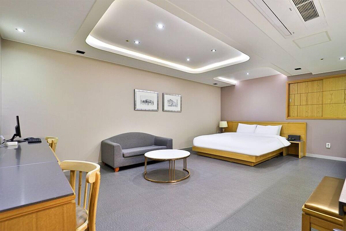 A hotel room with a bed, a desk, a chair, a small table, and a sofa.