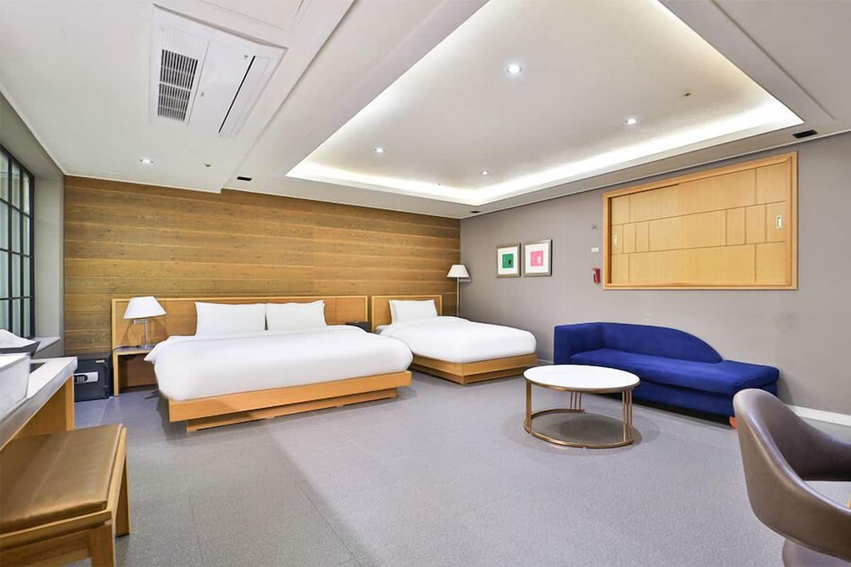 A modern hotel room with two beds, a sofa, a desk, and a chair.