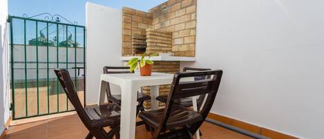 A small patio with a table and chairs, a potted plant, and a brick wall.