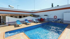 Una piscina con agua azul, rodeada de sillas de descanso y una mesa.