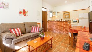 Una sala de estar con sofá, mesa de centro y una cocina con salpicadero de ladrillo y armarios de madera.