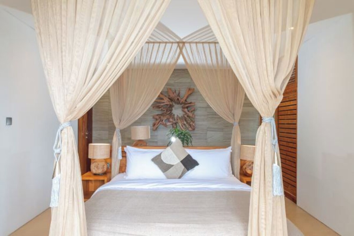 A bed with a canopy, a wall-mounted decorative piece, and two bedside tables with lamps.