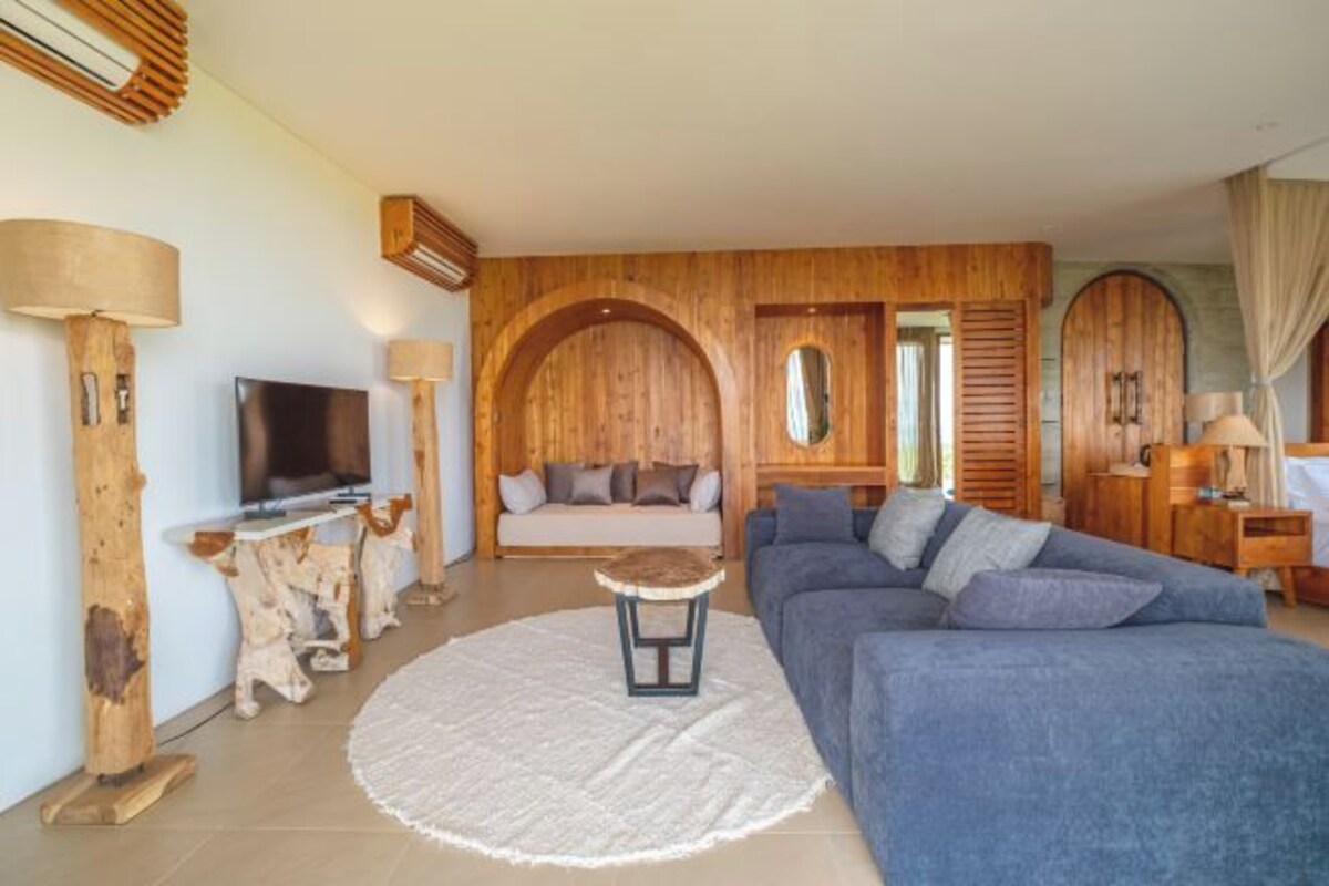 A modern living room with a large sofa, a TV, wooden decor, and a round rug.